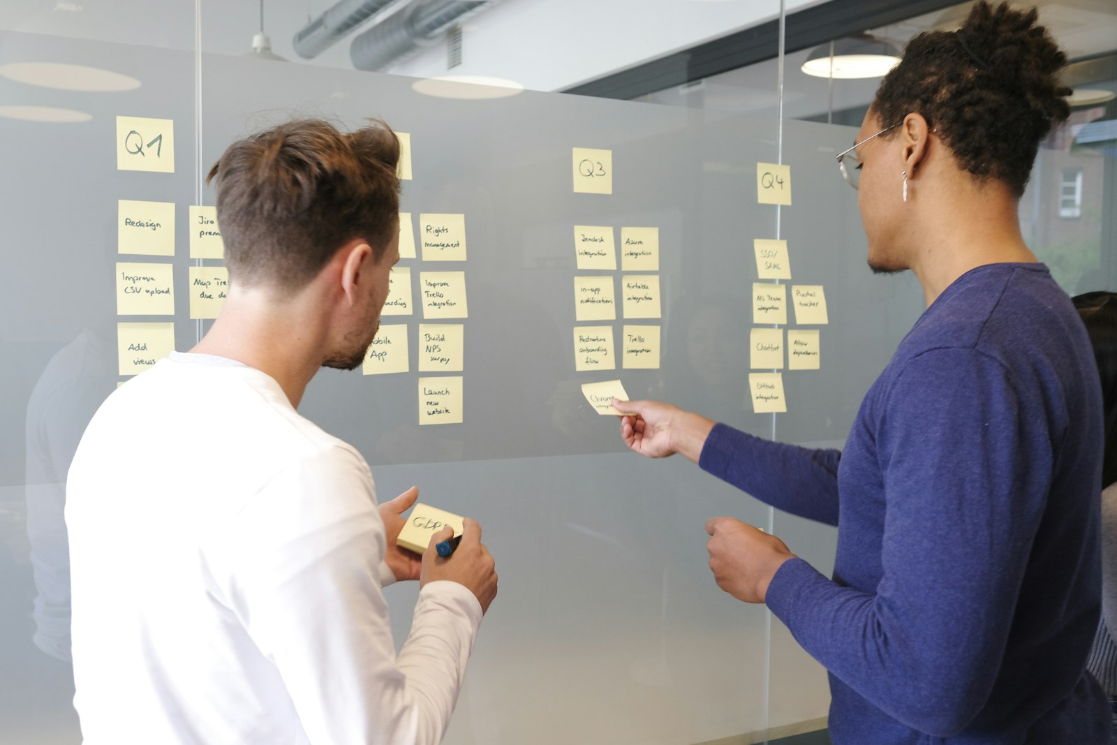 Two colleagues planning a project with sticky notes on a glass wall