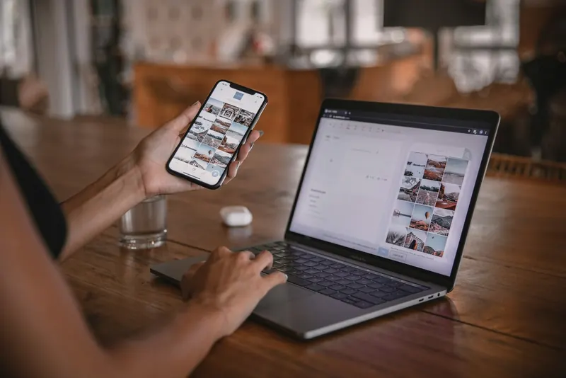 Person using a smartphone and a laptop at a table